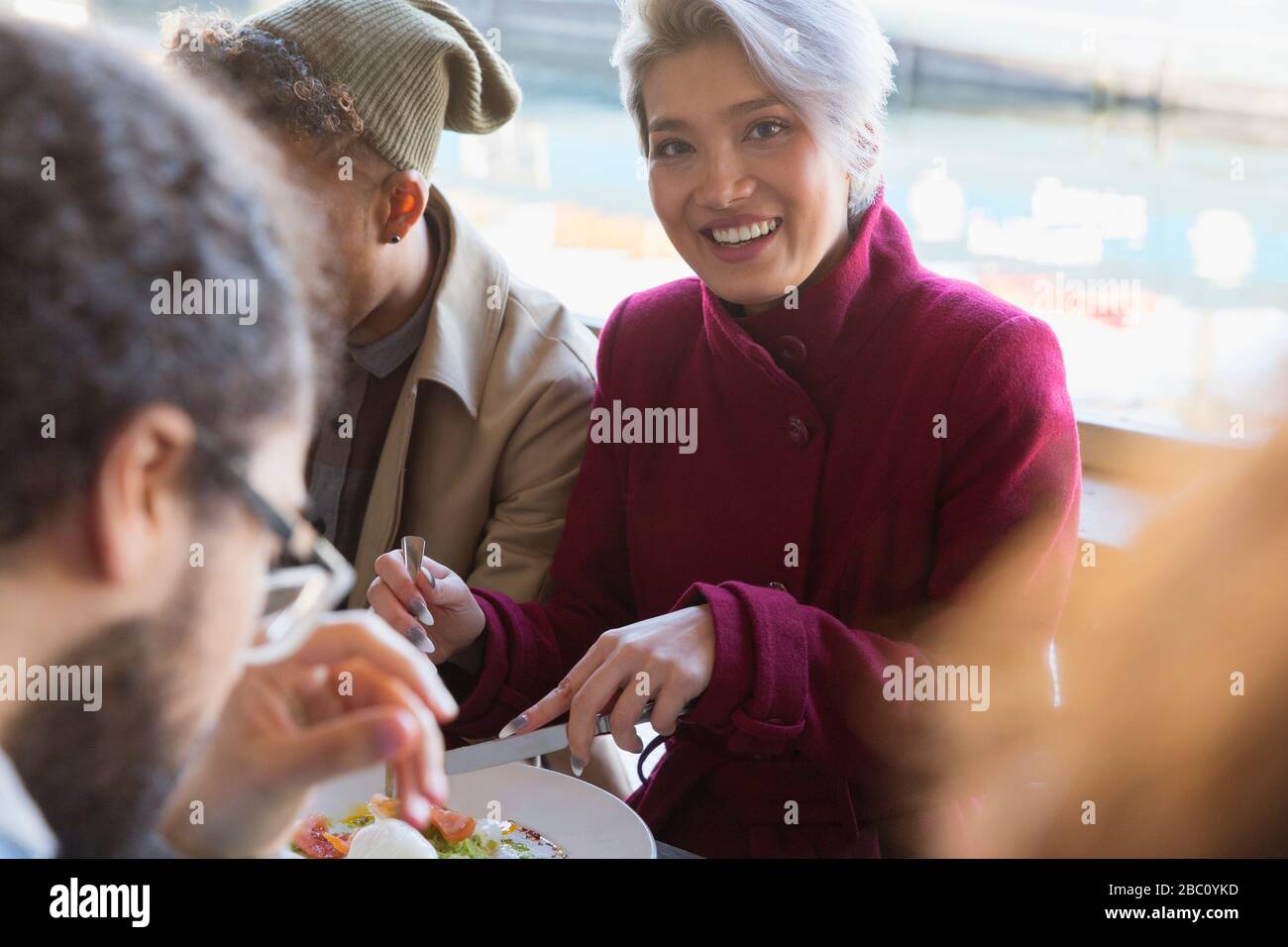 Portrait lächelnde junge Frau, die mit Freunden im Restaurant isst Stockfoto