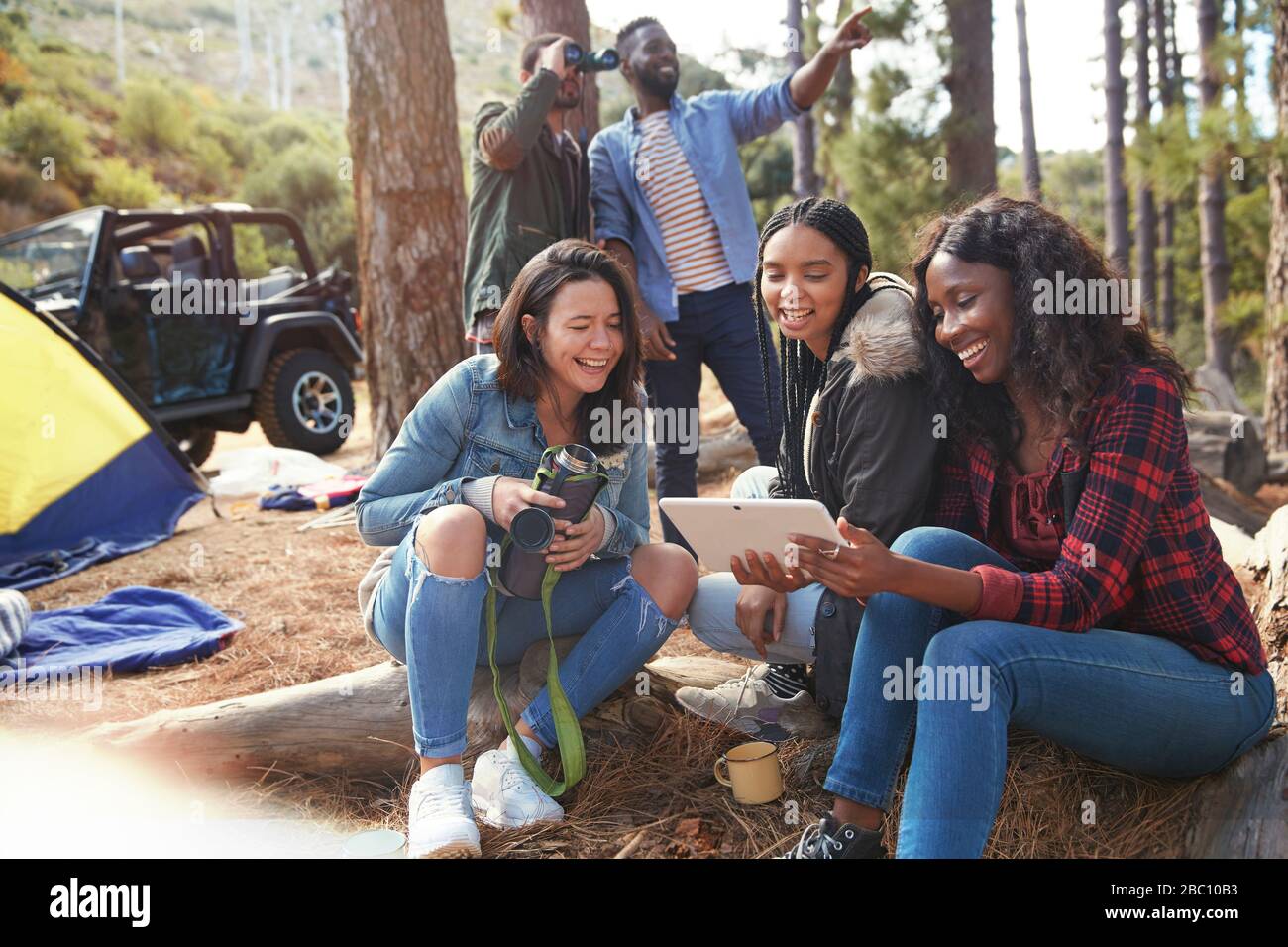 Lächelnde junge Frauen Freunde, die ein digitales Tablet auf dem Zeltplatz nutzen Stockfoto