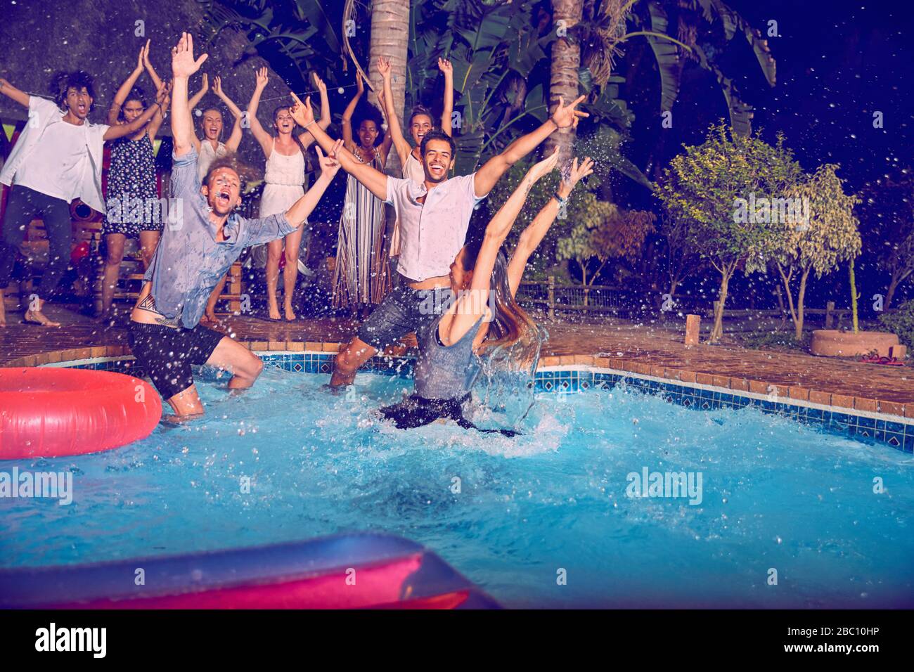 Portrait überschwängliche junge Freunde, die nachts in den Swimmingpool springen Stockfoto