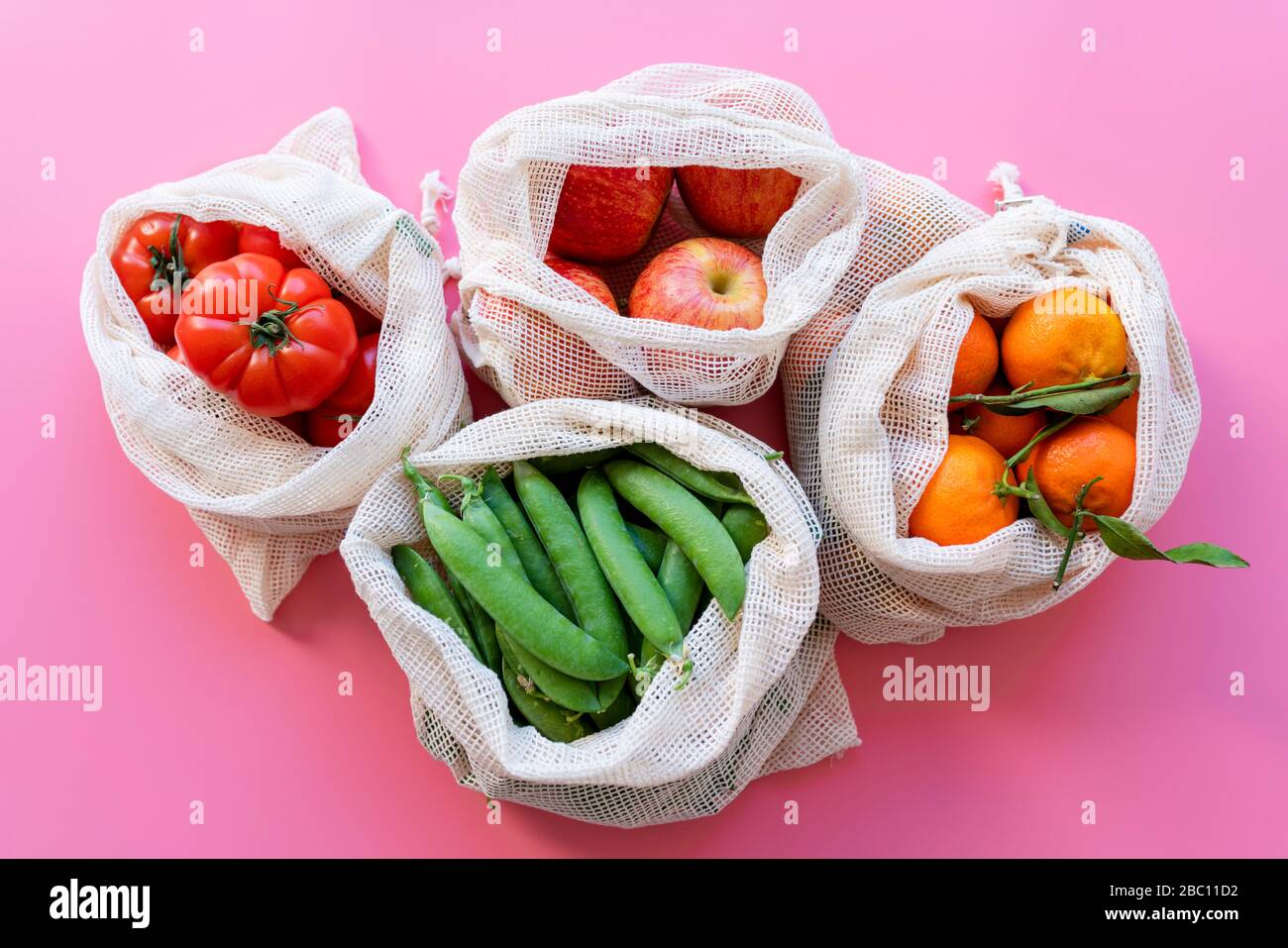 Umweltfreundliche wiederverwendbare Netzbeutel mit frischen grünen Erbsen, Tomaten, Äpfeln und Clementinen Stockfoto