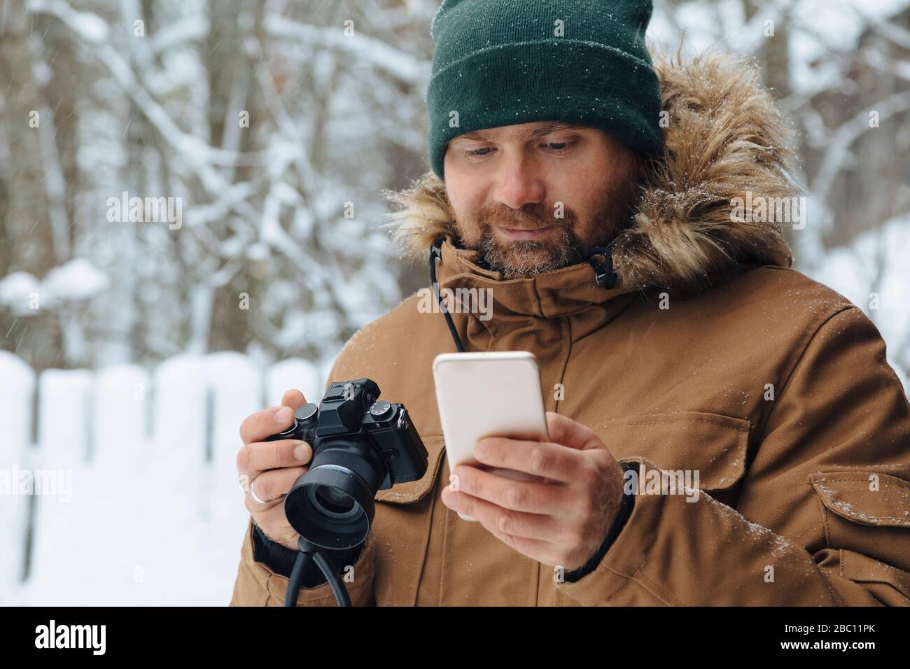Porträt des bärtigen Mannes mit Digitalkamera Blick auf Handy im Winter suchen Stockfoto