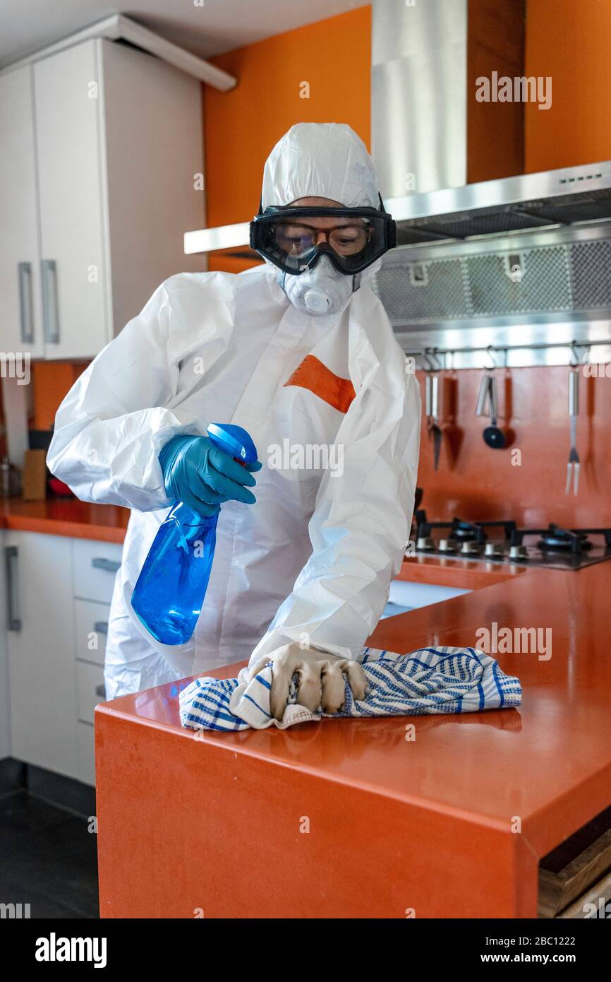 Frau, die Schutzkleidung trägt und ihre Küche desinfiziert Stockfoto