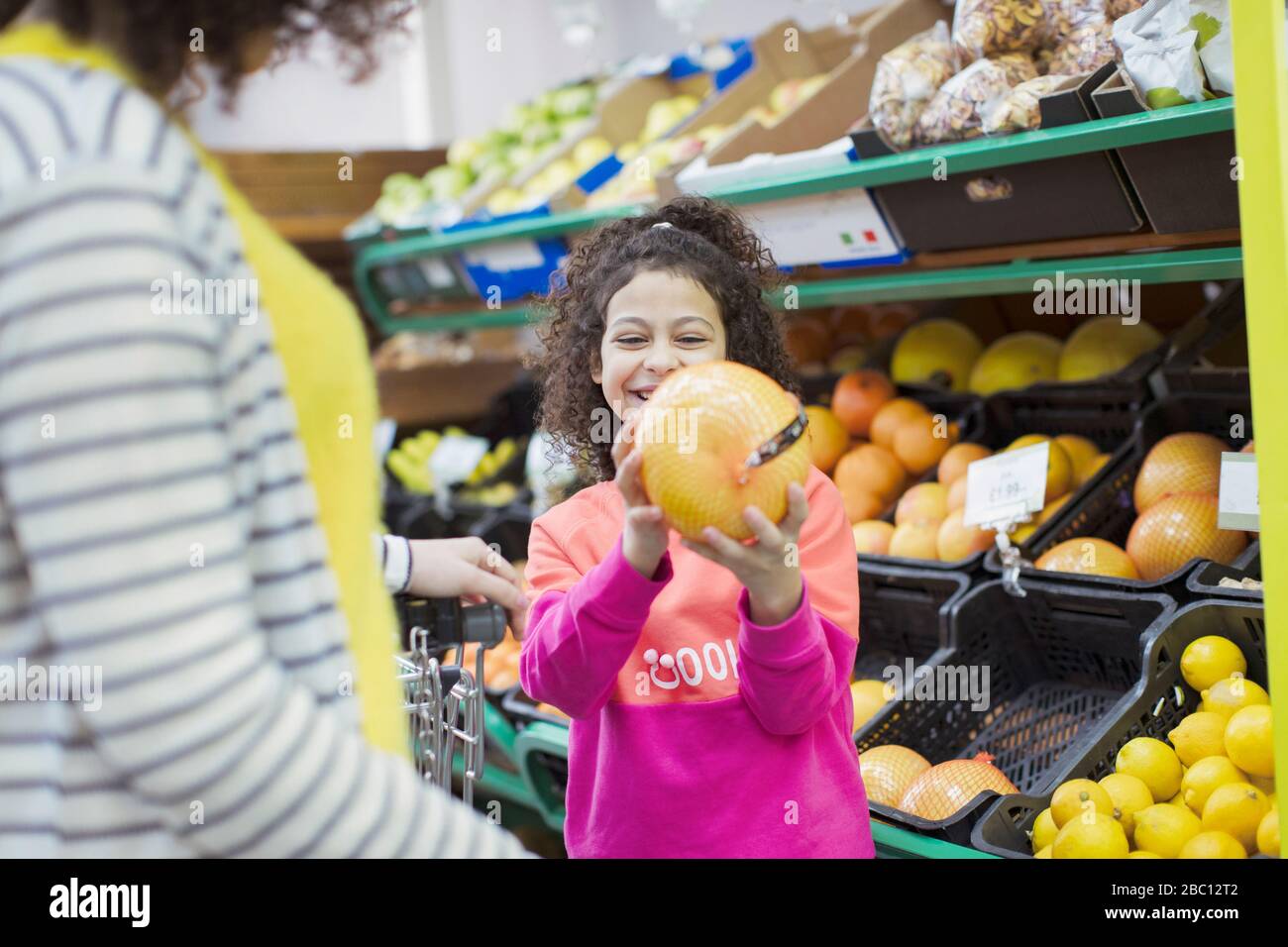 Lächelnde Tochter, die Grapefruit zur Mutter im Supermarkt zeigt Stockfoto