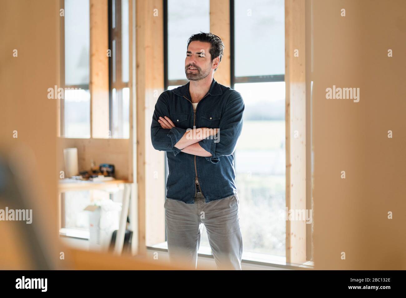Geschäftsmann steht am Fenster in einem offenen Büro aus Holz Stockfoto