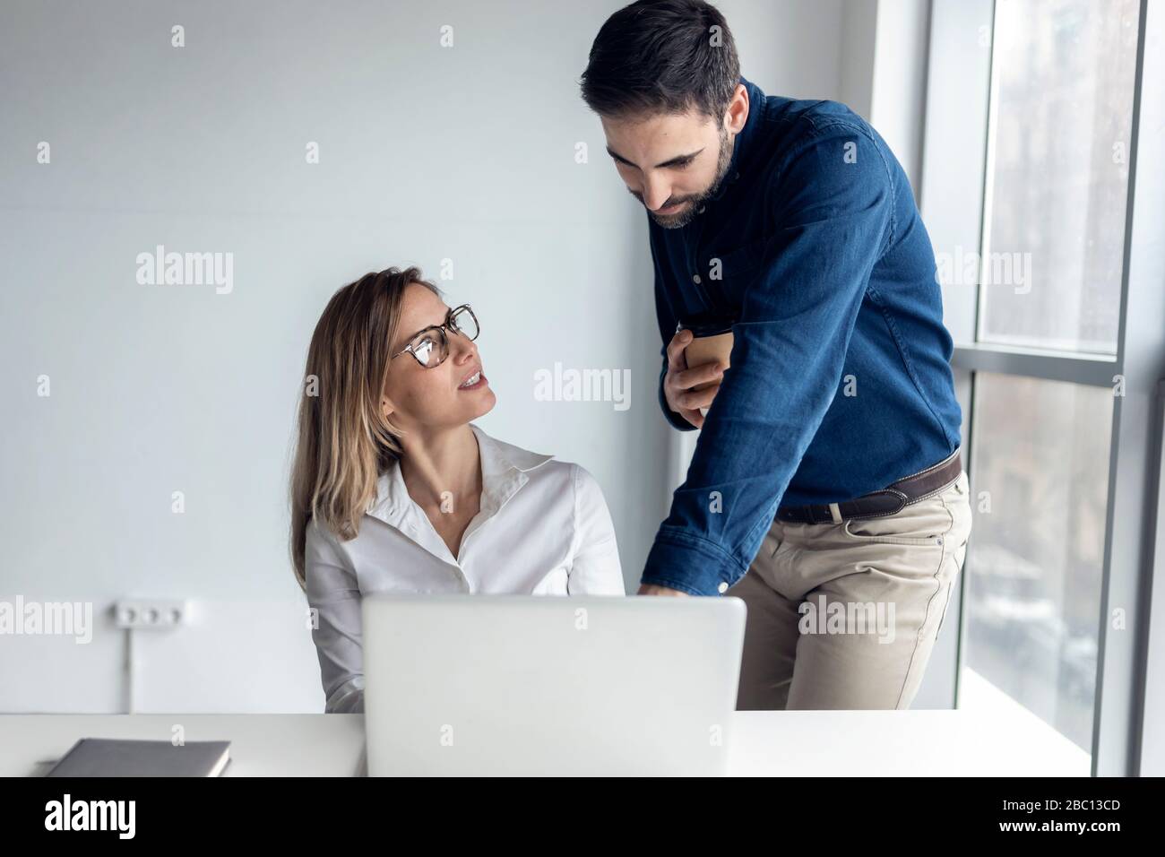 Geschäftsfrau sitzt am Schreibtisch und diskutiert mit ihrem Kollegen über die Arbeit Stockfoto