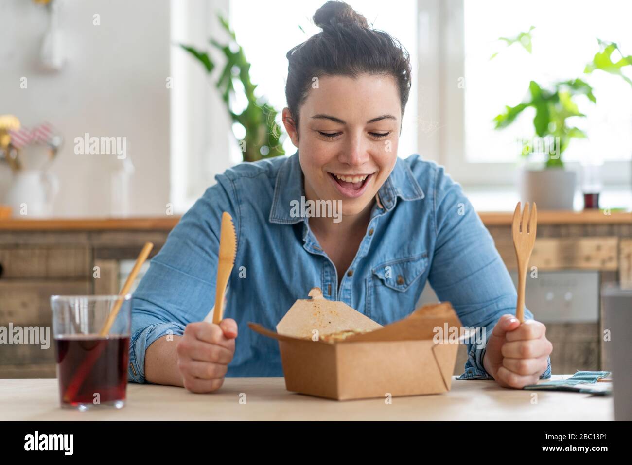 Porträt einer Frau, die am Tisch sitzt und mit Holzbesteck isst Stockfoto