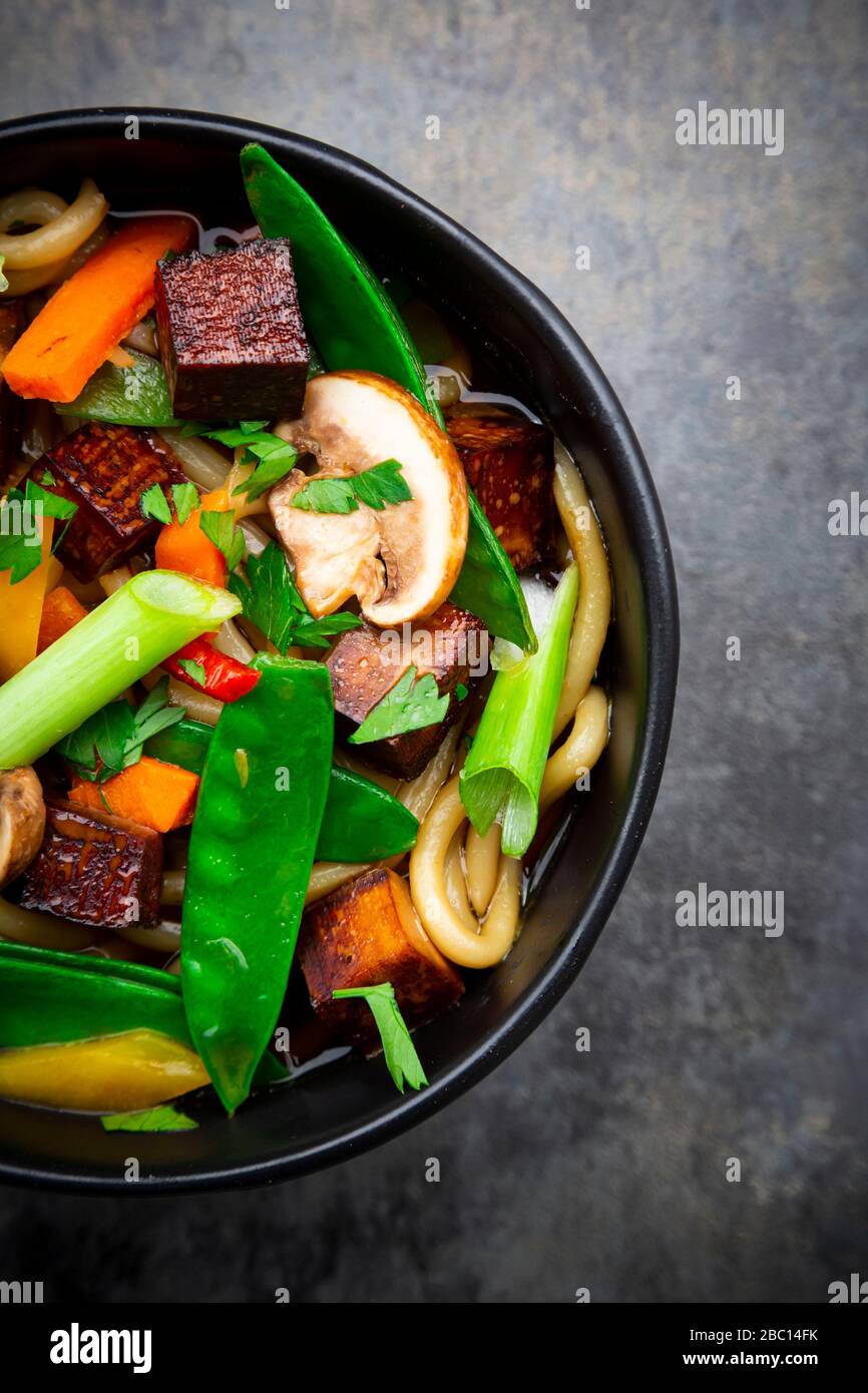 Schüssel mit verzehrfertigen Miso-Suppe mit udon-Nudeln, Tofu, Zuckererbsen, Paprika, Karotten, Mu-Err-Pilzen, Kopfzbarren und Koriander Stockfoto