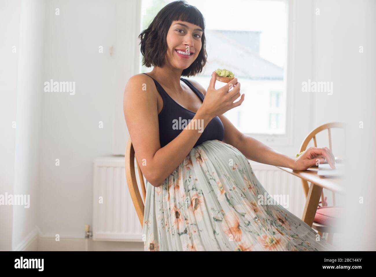 Portrait fröhliche schwangere Frau, die Avocado Toast isst Stockfoto