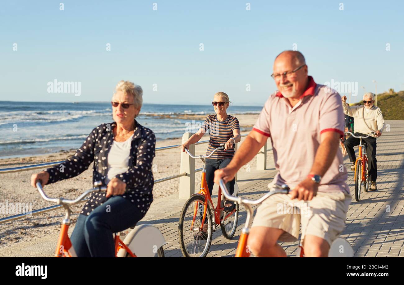 Aktive ältere Freunde fahren mit dem Fahrrad auf einem sonnigen Strandspaziergang entlang des Ozeans Stockfoto