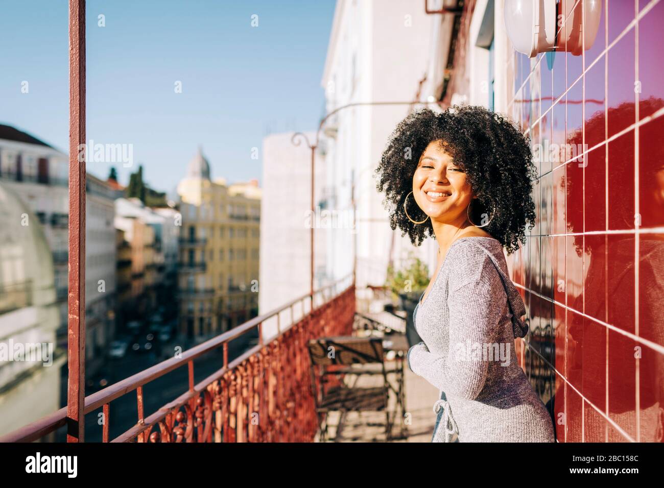 Porträt der glücklichen jungen Frau mit lockigen Haaren auf dem Balkon Stockfoto