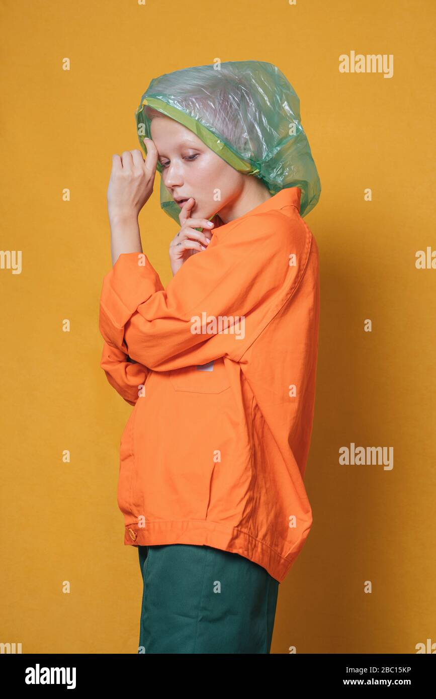 Porträt einer jungen Frau mit Plastiktüte auf dem Kopf trägt orange Jacke vor gelbem Hintergrund Stockfoto