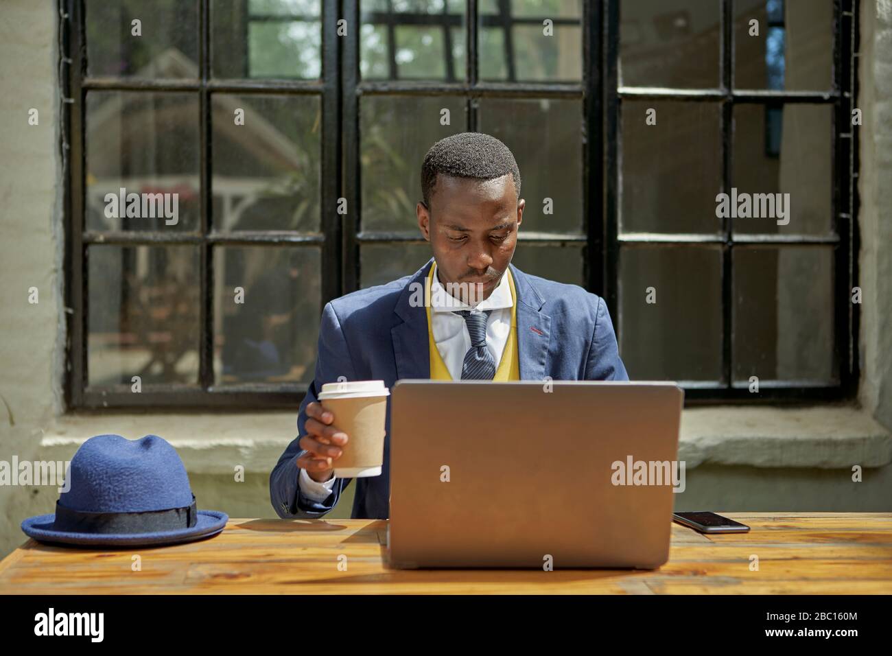 Ein eleganter junger Geschäftsmann, der in einem Café im Freien einen altmodischen Anzug mit Laptop trägt Stockfoto