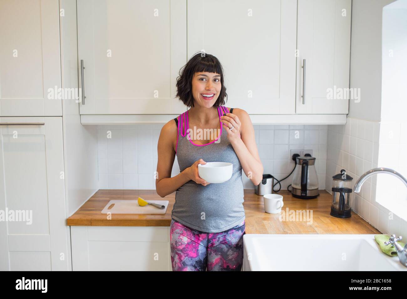 Portrait fröhliche schwangere Frau, die in der Küche isst Stockfoto