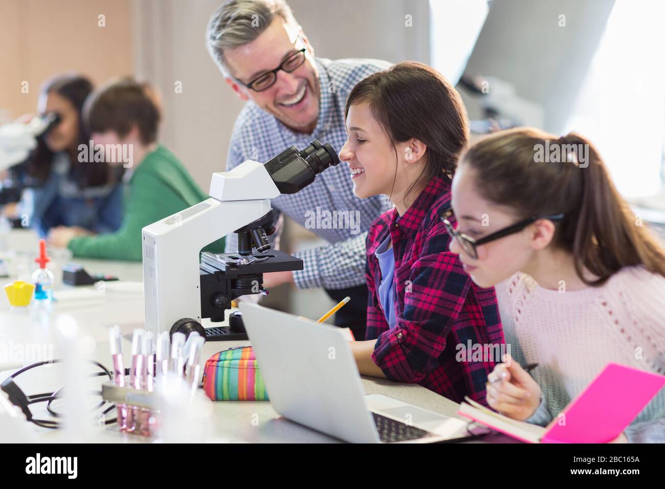 Lächelnde wissenschaftliche Lehrerin, die Mädchen bei wissenschaftlichen Experimenten am Mikroskop im Labor hilft Stockfoto