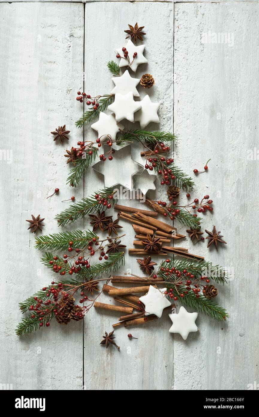 Sternförmige Plätzchen, Zimtstangen, Tannenzweige, Sternanis, Ausstechformen, Tannenzapfen und Hagebutten in Form eines Weihnachtsbaums angeordnet Stockfoto