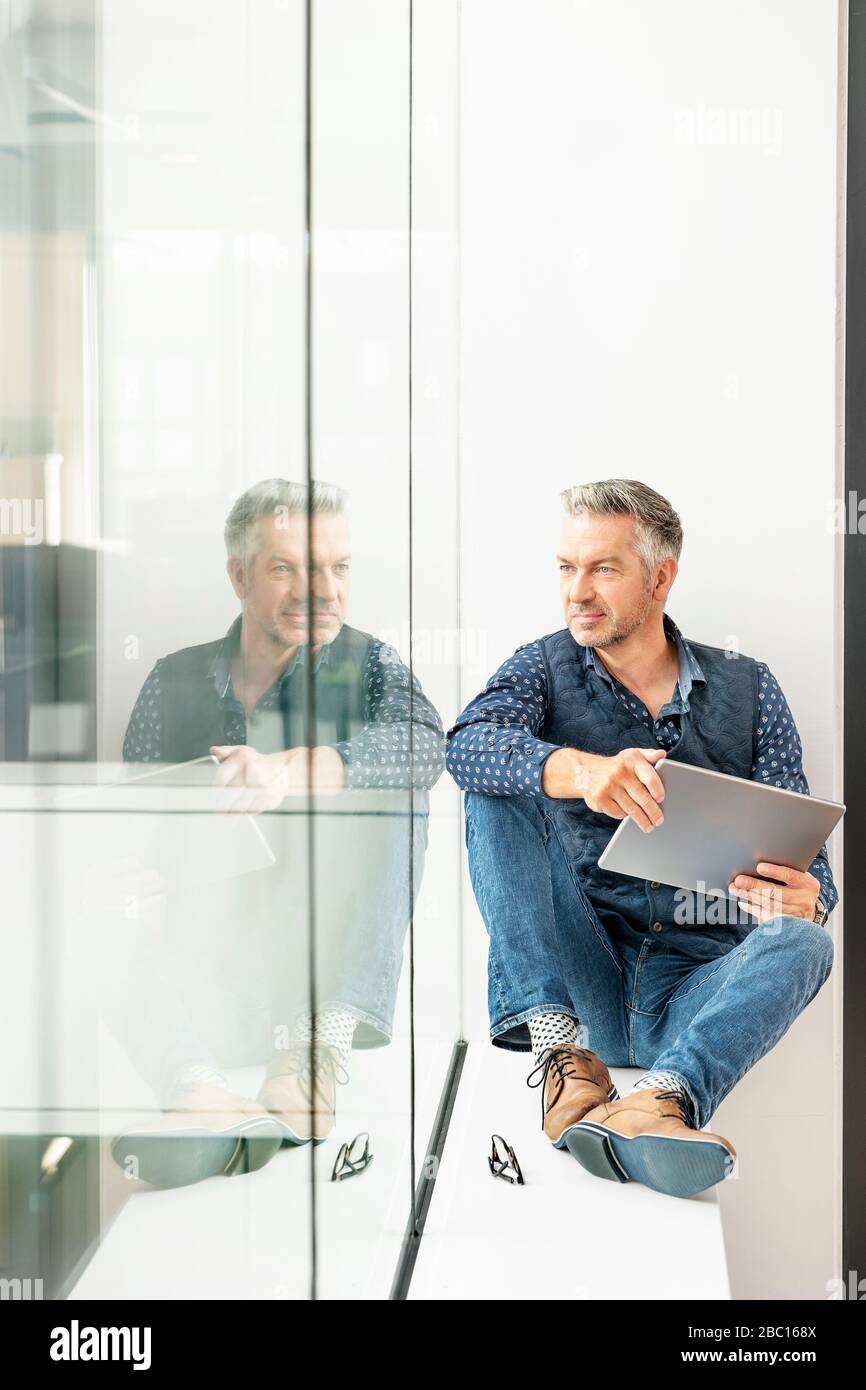 Zwangloser Geschäftsmann sitzt auf Fensterbank im Bürogebäude, mit Laptp Stockfoto