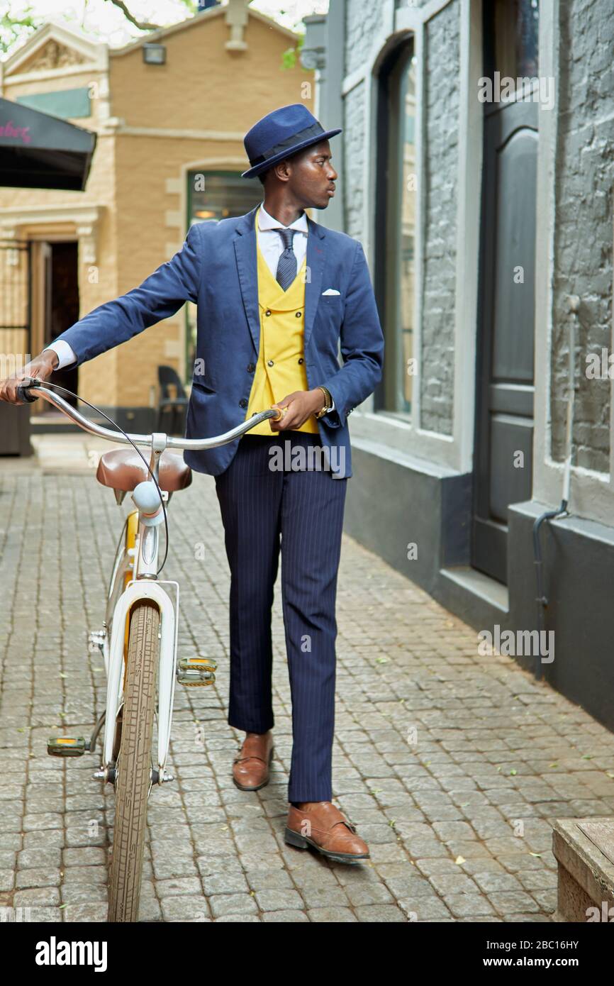 Stilvoller junger Geschäftsmann mit Fahrrad in altmodischem Anzug, der eine Gasse entlang läuft Stockfoto