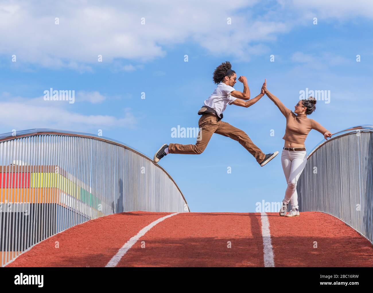 Mann springt mitten in der Luft auf Brücke, hochfivende Frau Stockfoto
