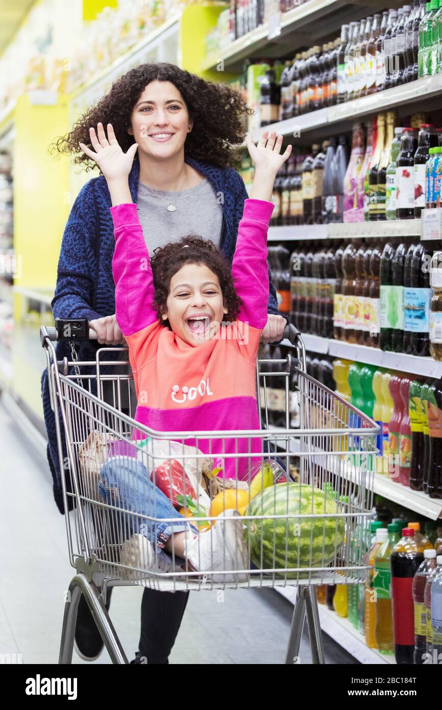 Mutter treibt aufgeregte Tochter in den Einkaufswagen im Supermarkt Gang Stockfoto