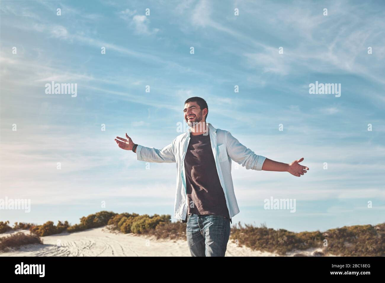 Überschwänglicher junger Mann mit Armen am sonnigen Strand ausgestreckt Stockfoto