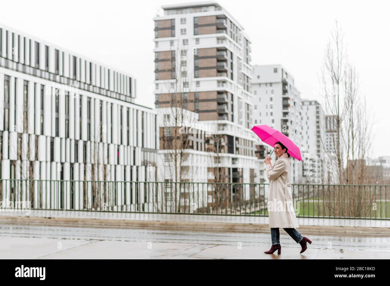 Lächelnde Frau mit rosa Regenschirm zu Fuß in der Stadt Stockfoto