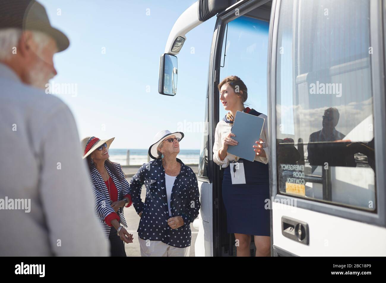 Reiseleiter im Gespräch mit aktiven Seniorentouristen am Eingang des Reisebus Stockfoto