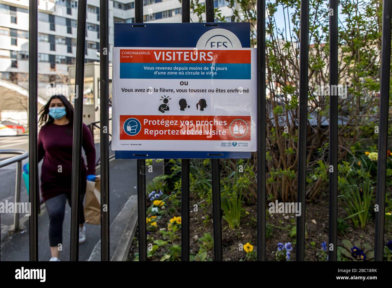 POSTER FÜR DIE SYMPTOME VON COVID-19 UND PATIENT MIT MASKE UND HANDSCHUHEN, DIE DAS KRANKENHAUS SAINT ANTOINE, PARIS, ILE-DE-FRANCE VERLASSEN Stockfoto