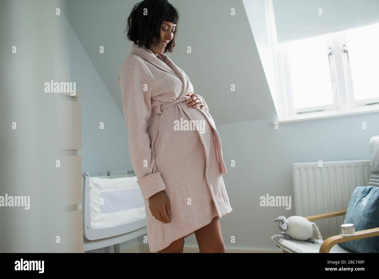 Glückliche schwangere Frau im bademantel reibt Magen Stockfoto