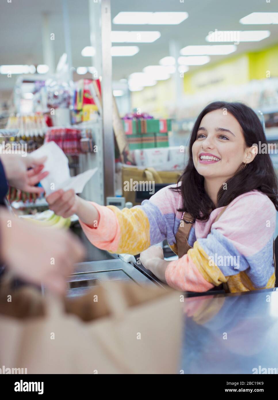Lächelnde, freundliche Kassiererin, die dem Kunden an der Kasse des Supermarktes den Empfang gibt Stockfoto