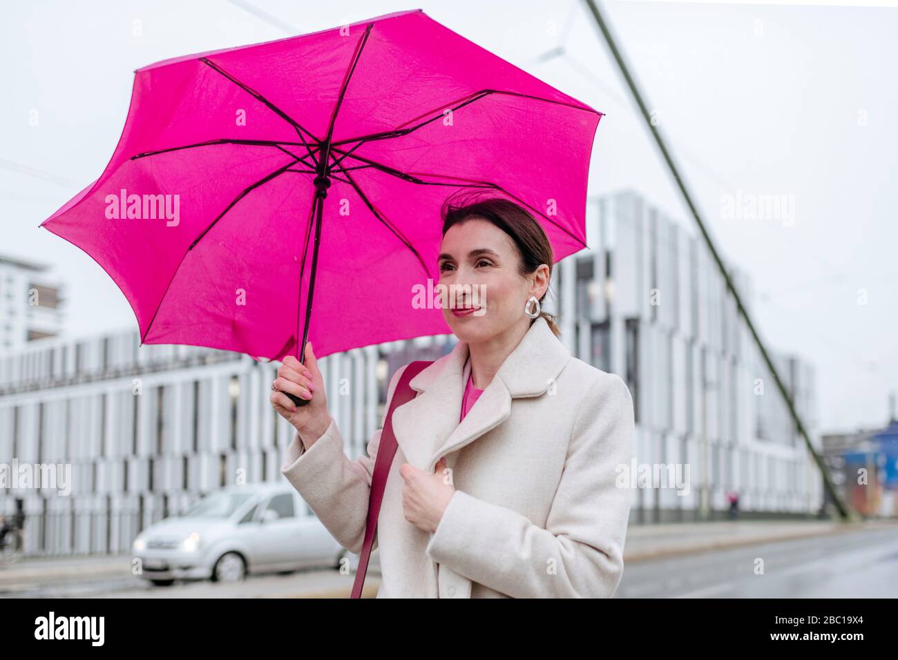 Lächelnde Frau mit rosa Regenschirm zu Fuß in der Stadt Stockfoto