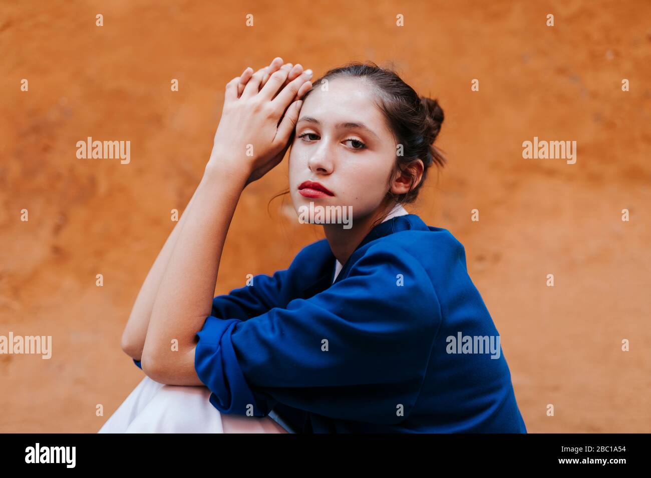 Porträt eines weiblichen Teenagers mit blauer Jacke vor einer braunen Wand Stockfoto