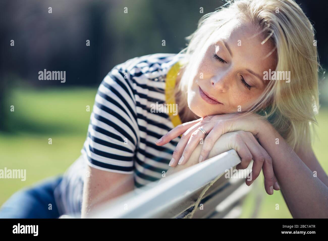 Blonde lächelnde Frau auf einer Bank sitzen und auf Kamera schauen Stockfoto