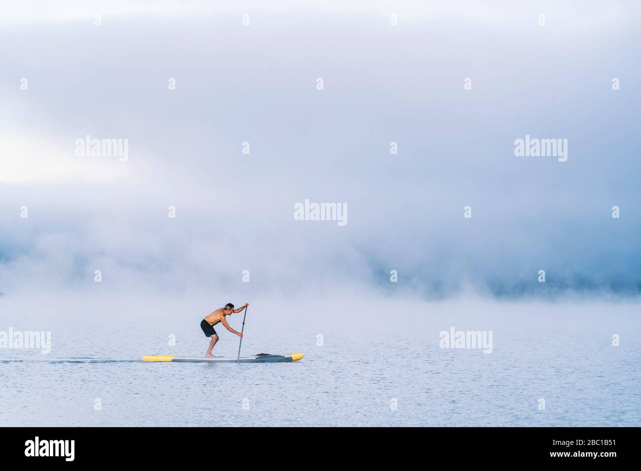 Mann steht auf Paddelsurfen auf einem See im Nebel Stockfoto