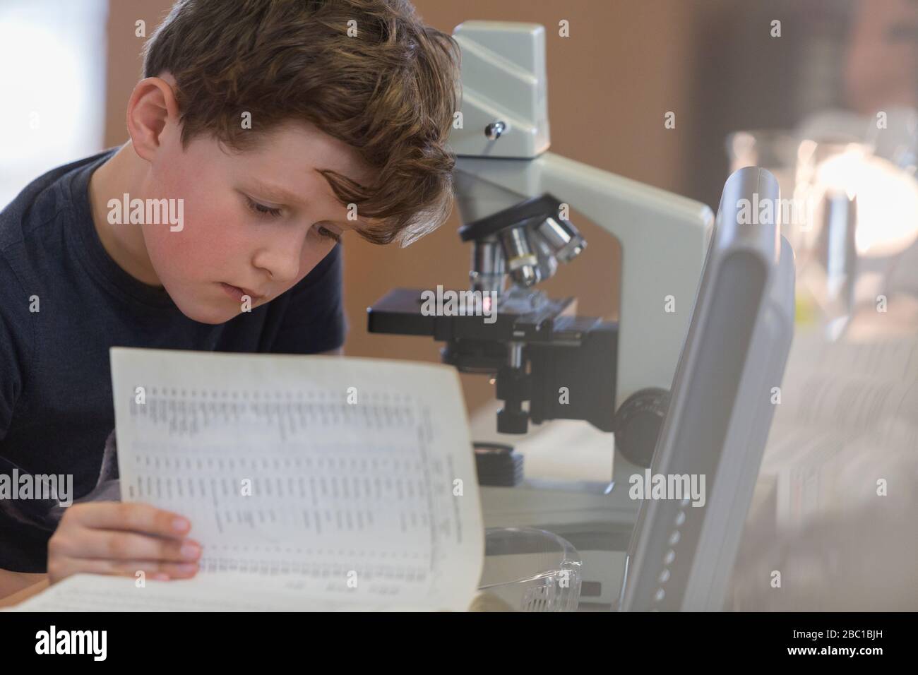 Schüler mit Schwerpunkt lesen Lehrbuch am Mikroskop im Laborunterricht Stockfoto