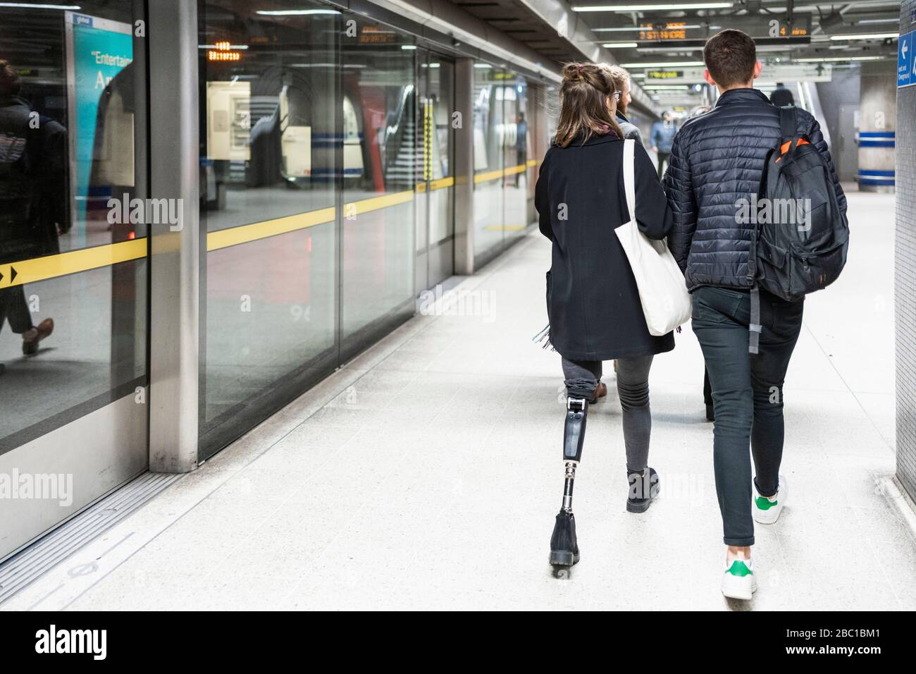 Rückansicht der jungen Frau mit Beinprothese und Mann zu Fuß an der U-Bahn-Station platfom Stockfoto