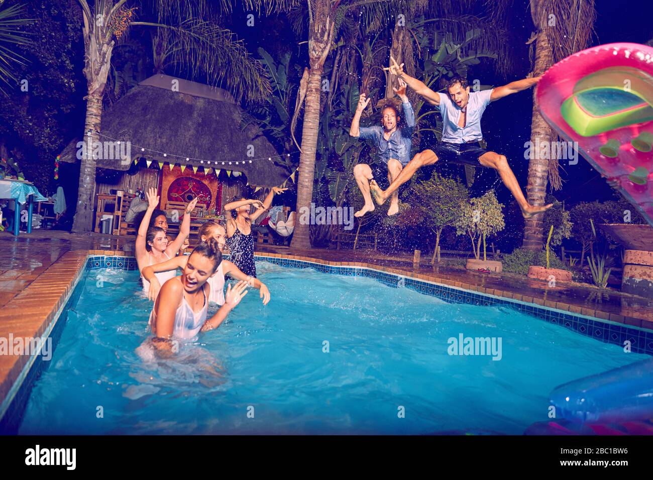 Überschwängliche junge Männerfreunde springen nachts in den Swimmingpool Stockfoto