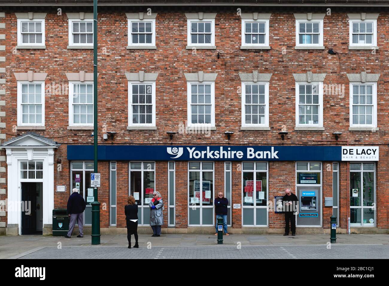 Die Leute warten geduldig auf die Bank, nachdem die meisten Geschäfte während des Ausbruchs des Corona-Virus in Beverley, Yorkshire, Großbritannien geschlossen wurden. Stockfoto