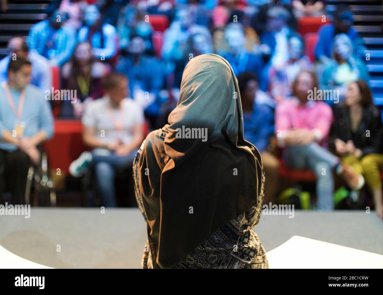 Weibliche Sprecherin im Hijab auf der Bühne, die mit dem Publikum spricht Stockfoto