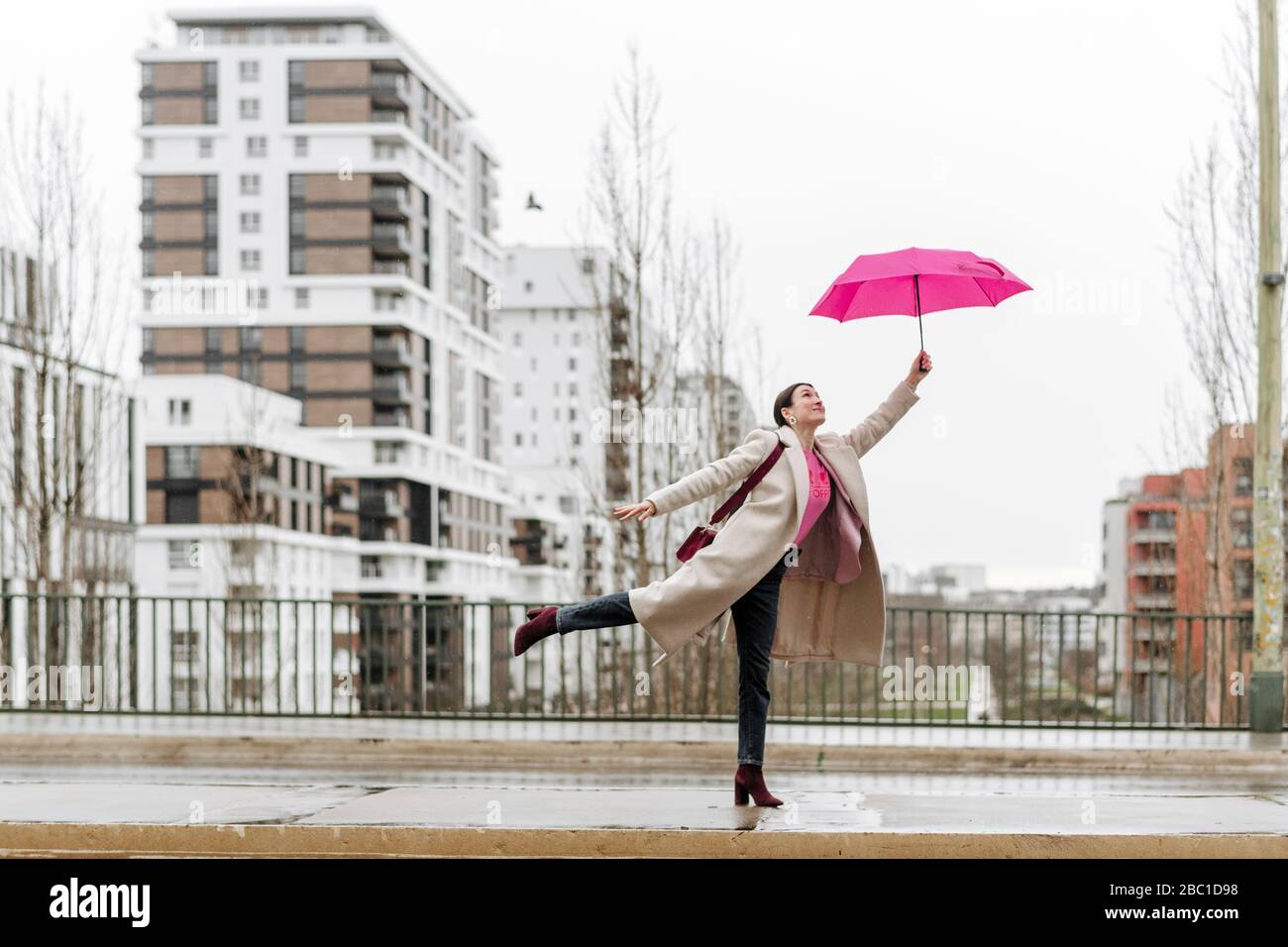 Lächelnde Frau mit rosa Regenschirm zu Fuß in der Stadt Stockfoto