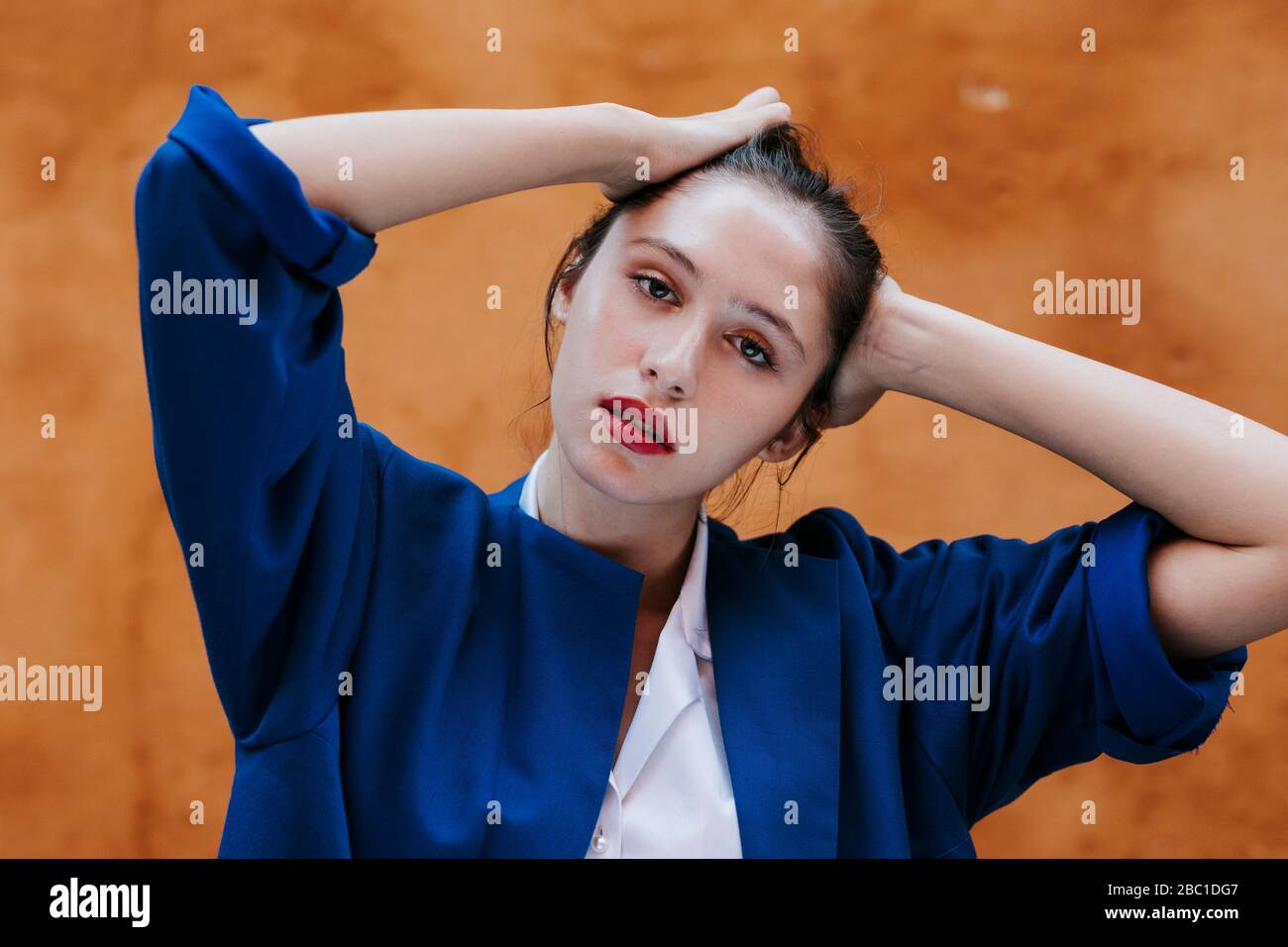 Porträt eines weiblichen Teenagers mit blauer Jacke vor einer braunen Wand Stockfoto