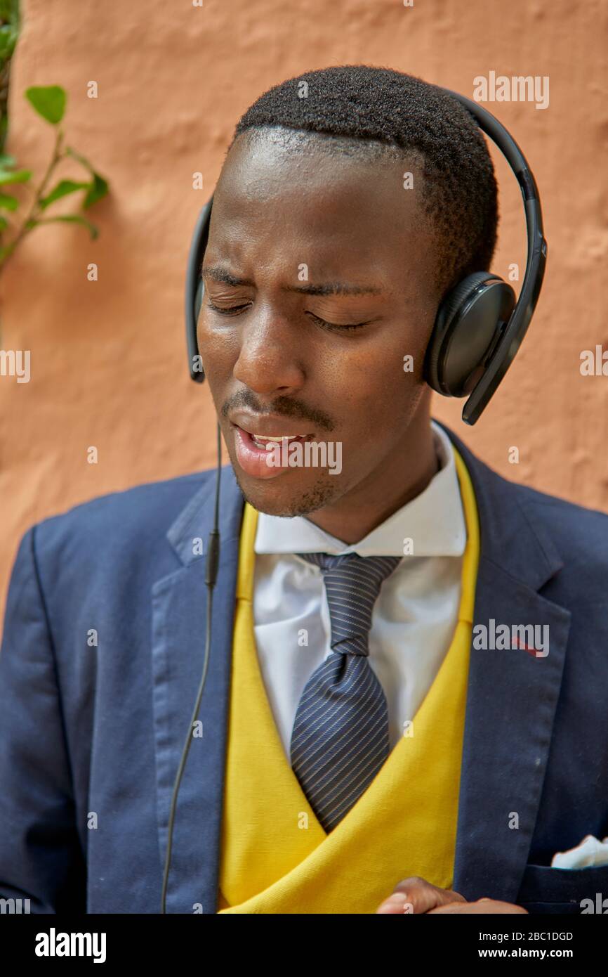 Stilvoller junger Geschäftsmann in altmodischem Anzug, der Musik über seine Kopfhörer hört Stockfoto