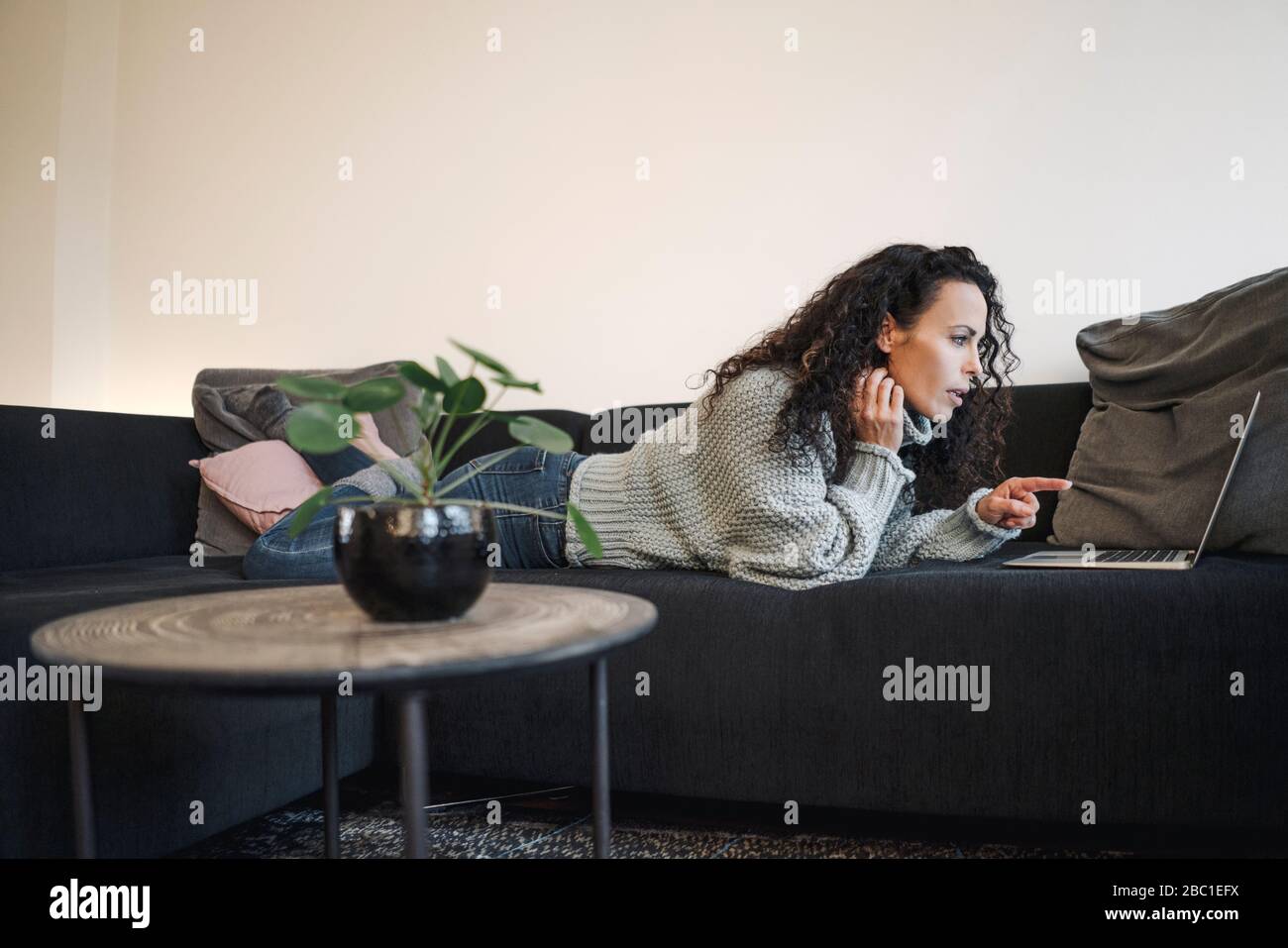 Frau auf der Couch liegend, Laptop verwendend, auf Bildschirm zeigend Stockfoto