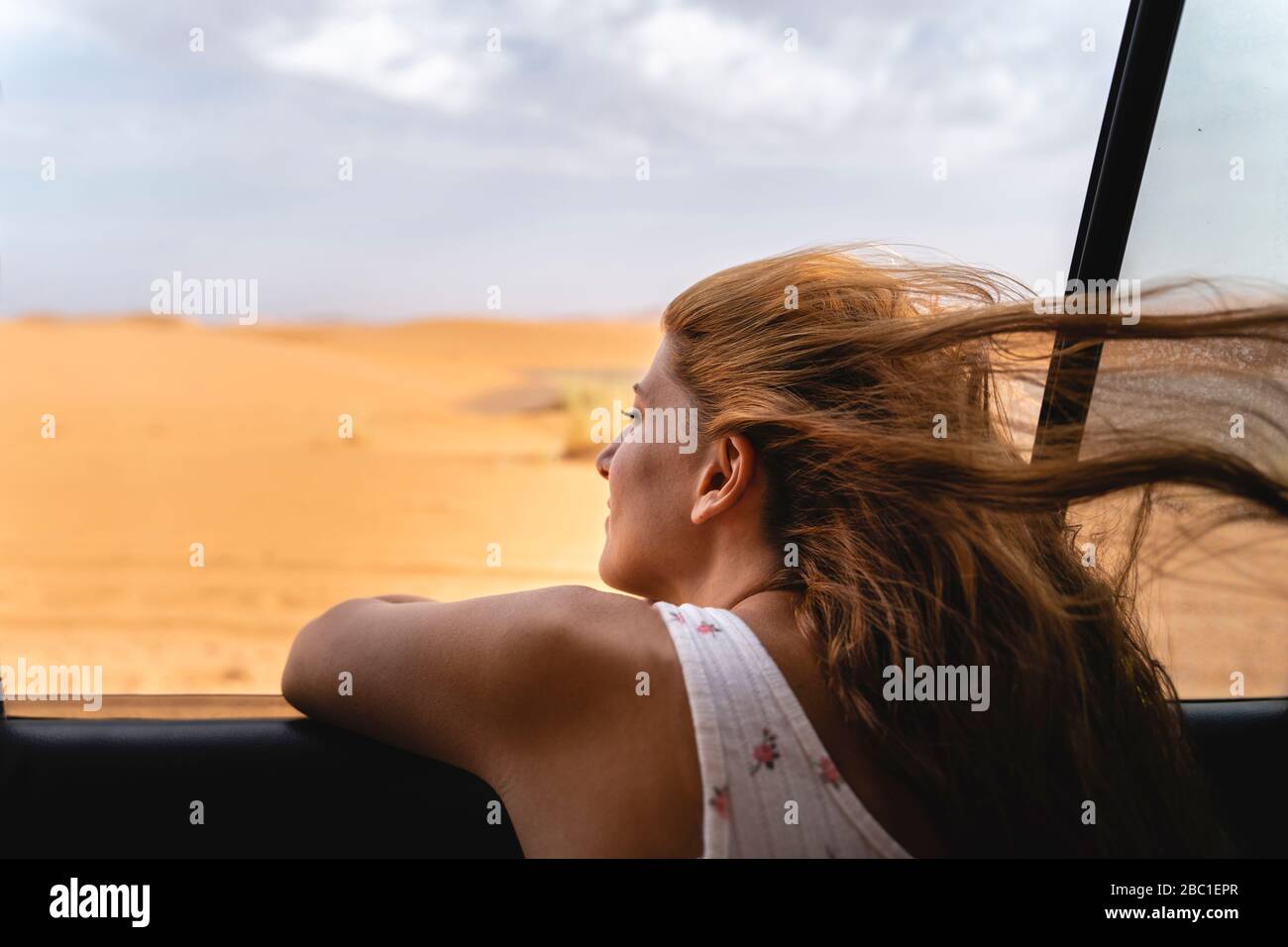 Junge Frau im Auto, die sich aus dem Fenster in der Sahara-Wüste, Merzouga, Marokko lehnt Stockfoto