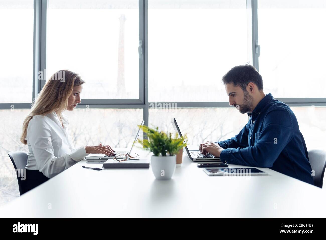 Geschäftsmann und Frau sitzen am Schreibtisch, benutzen Laptops, schauen ernsthaft Stockfoto
