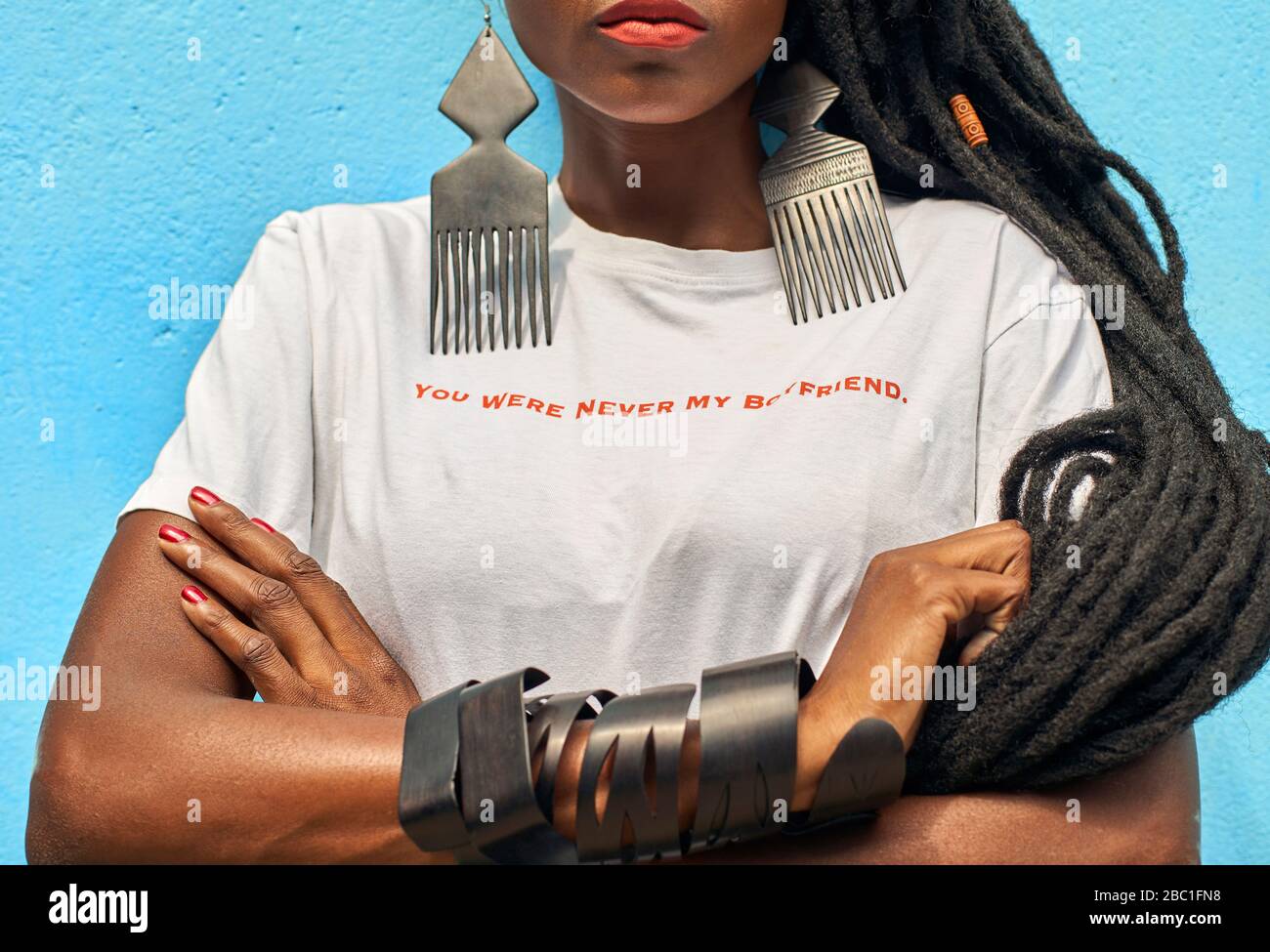 Porträt einer Frau mit langen Dreadlocks, die ein T-Shirt trägt und auf dem die Botschaft „Du warst nie mein Freund“ vor der türkisfarbenen Wand steht Stockfoto