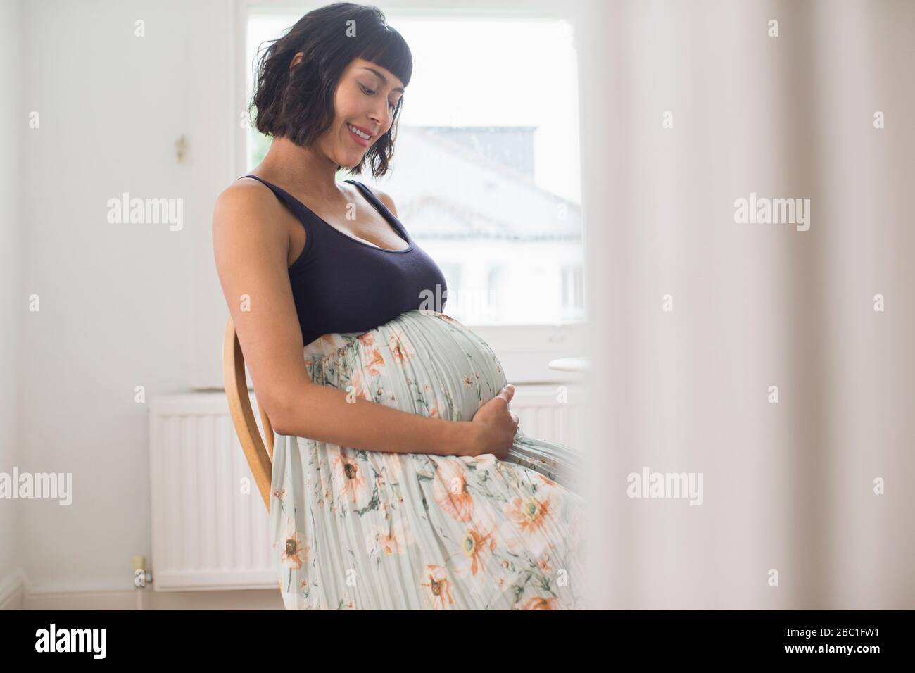 Glückliche schwangere Frau im Blumenkleid, das den Magen hält Stockfoto