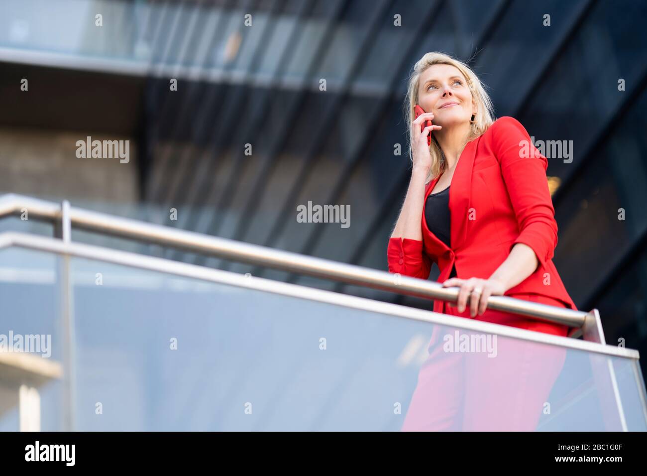 Blonde Geschäftsfrau in rotem Anzug und mit Smartphone Stockfoto