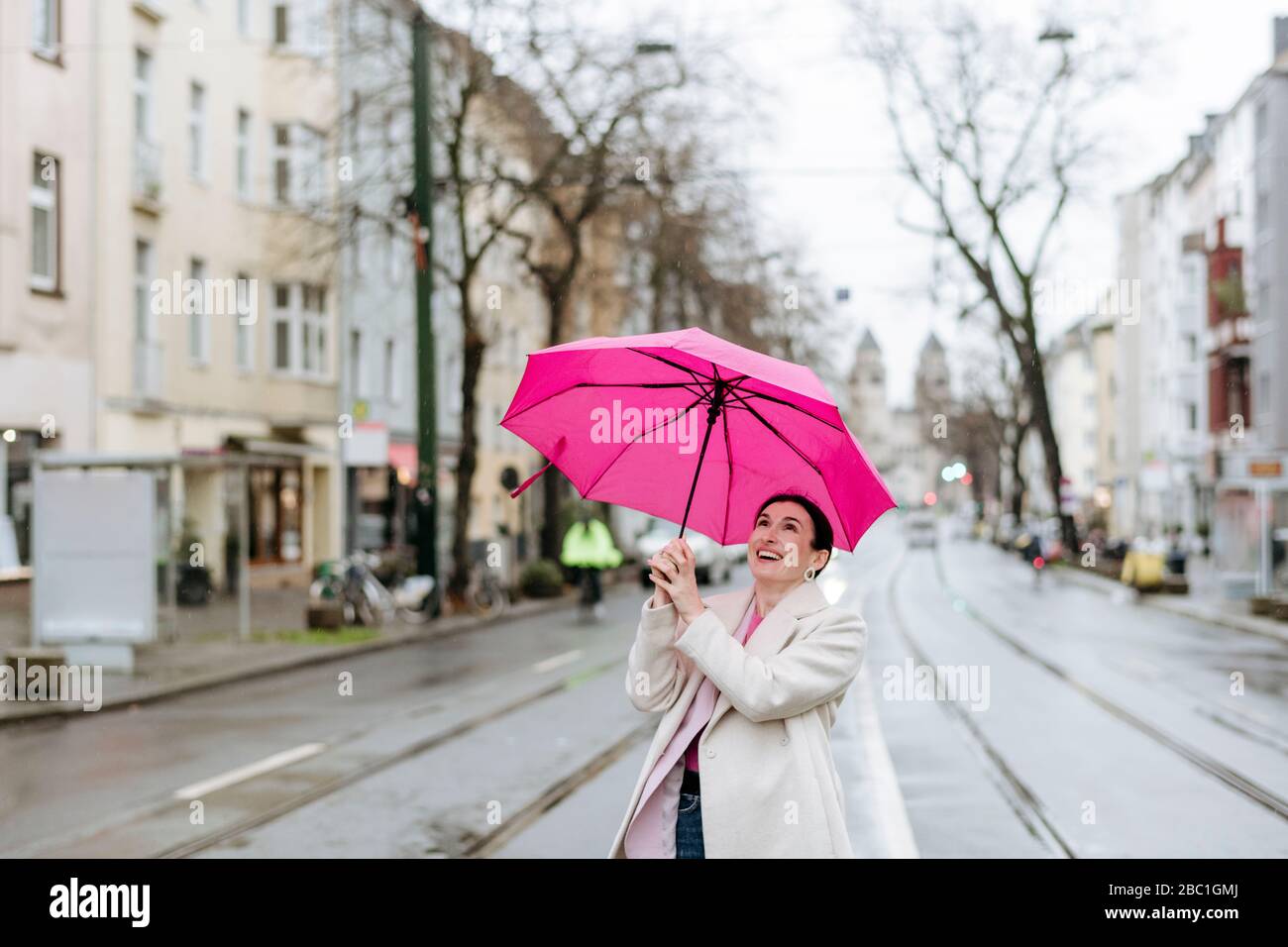 Lächelnde Frau mit rosa Regenschirm auf der Straße Stockfoto