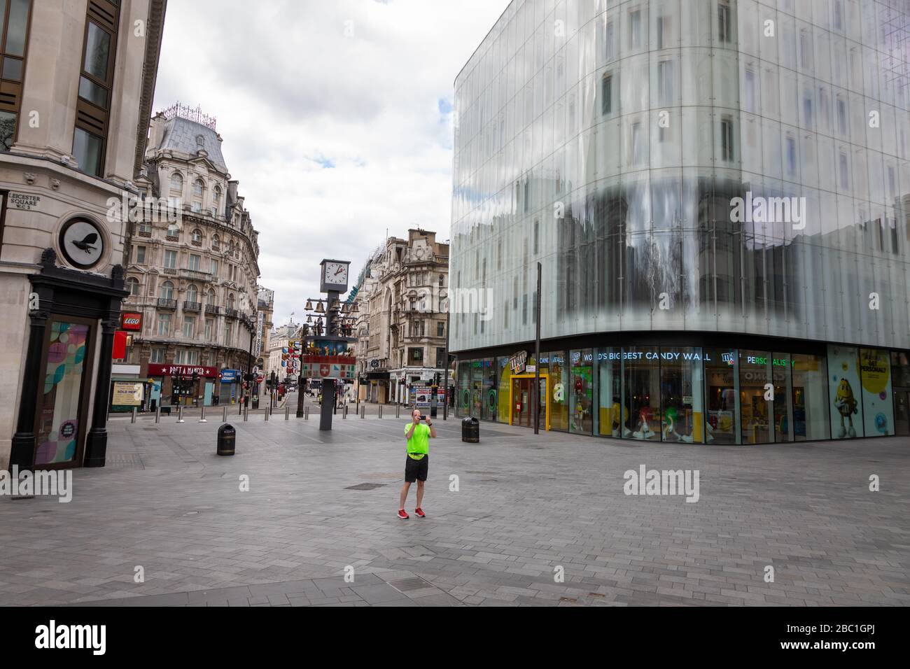 Ein menschenleerer Leicester Square in Central London während des Corona-Virus-Ausbruchs. Es gibt einen einsamen Läufer, der angehalten hat, Fotos zu machen. Stockfoto