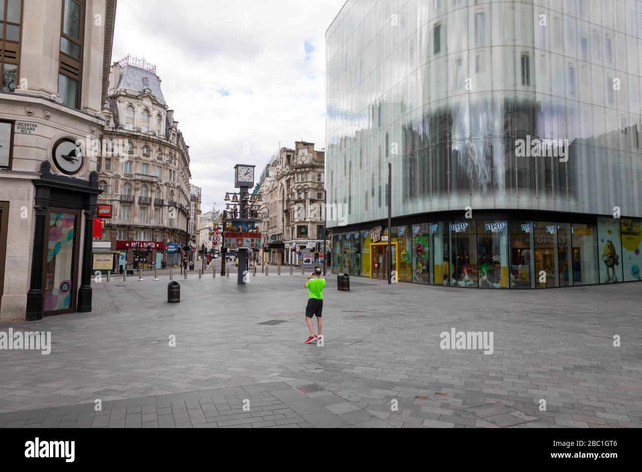 Ein menschenleerer Leicester Square in Central London während des Corona-Virus-Ausbruchs. Es gibt einen einsamen Läufer, der angehalten hat, Fotos zu machen. Stockfoto